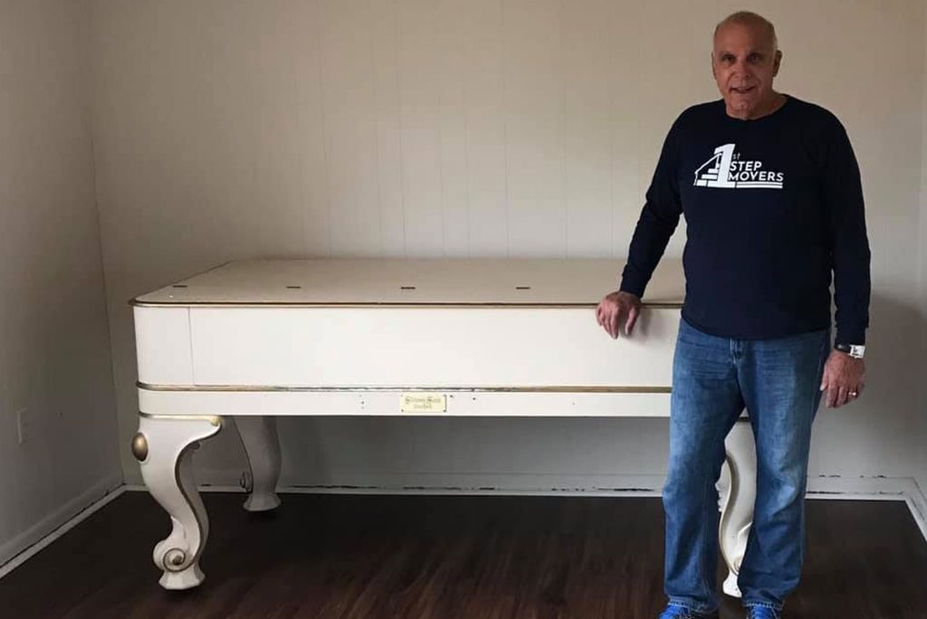 A 1st Step Movers team member beside an antique white piano in an empty room