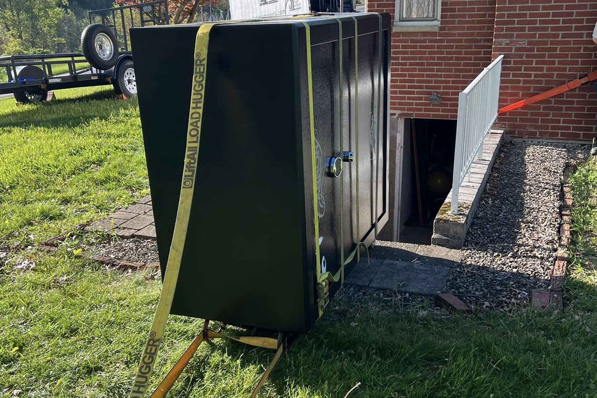 Gun safe strapped with yellow ratchet straps on a lawn beside a house, ready to move