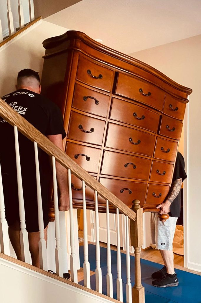 Two movers carrying a wooden dresser up a staircase
