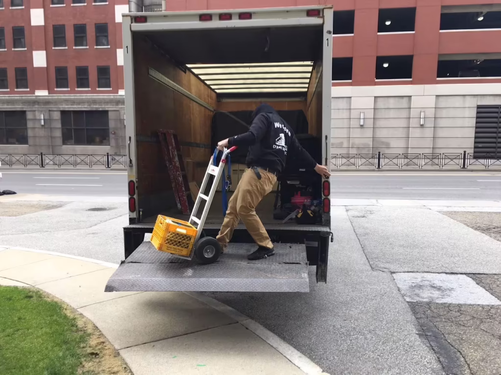 Mover using a hand truck to roll items up the lift gate into a 1st Step truck on a city street
